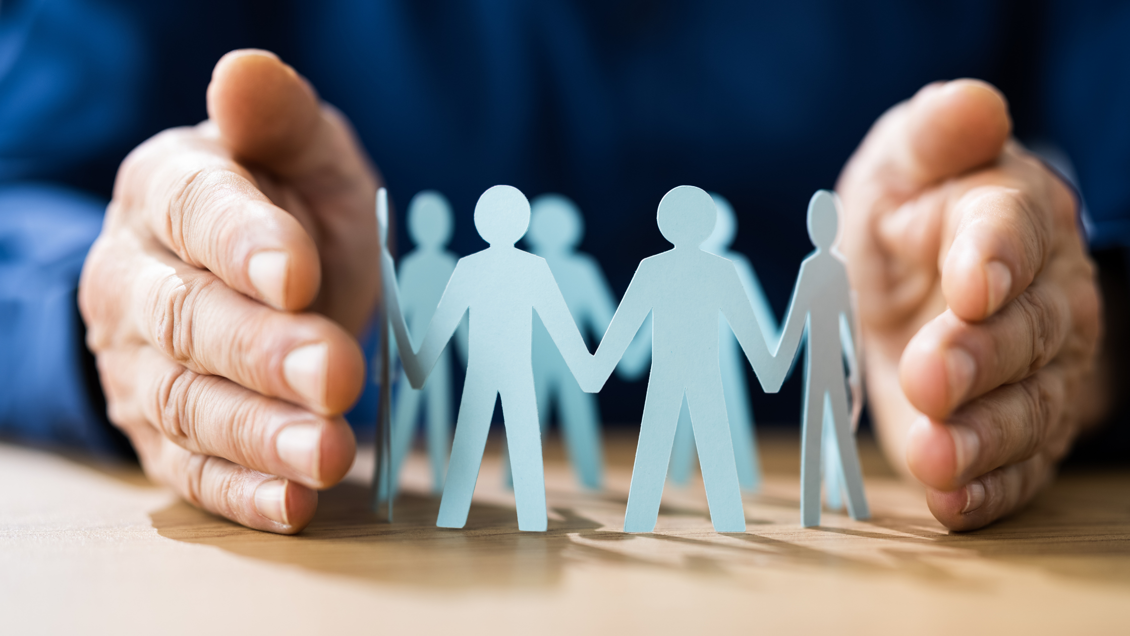 Hands protecting paper cutout figures representing employees during a business sale